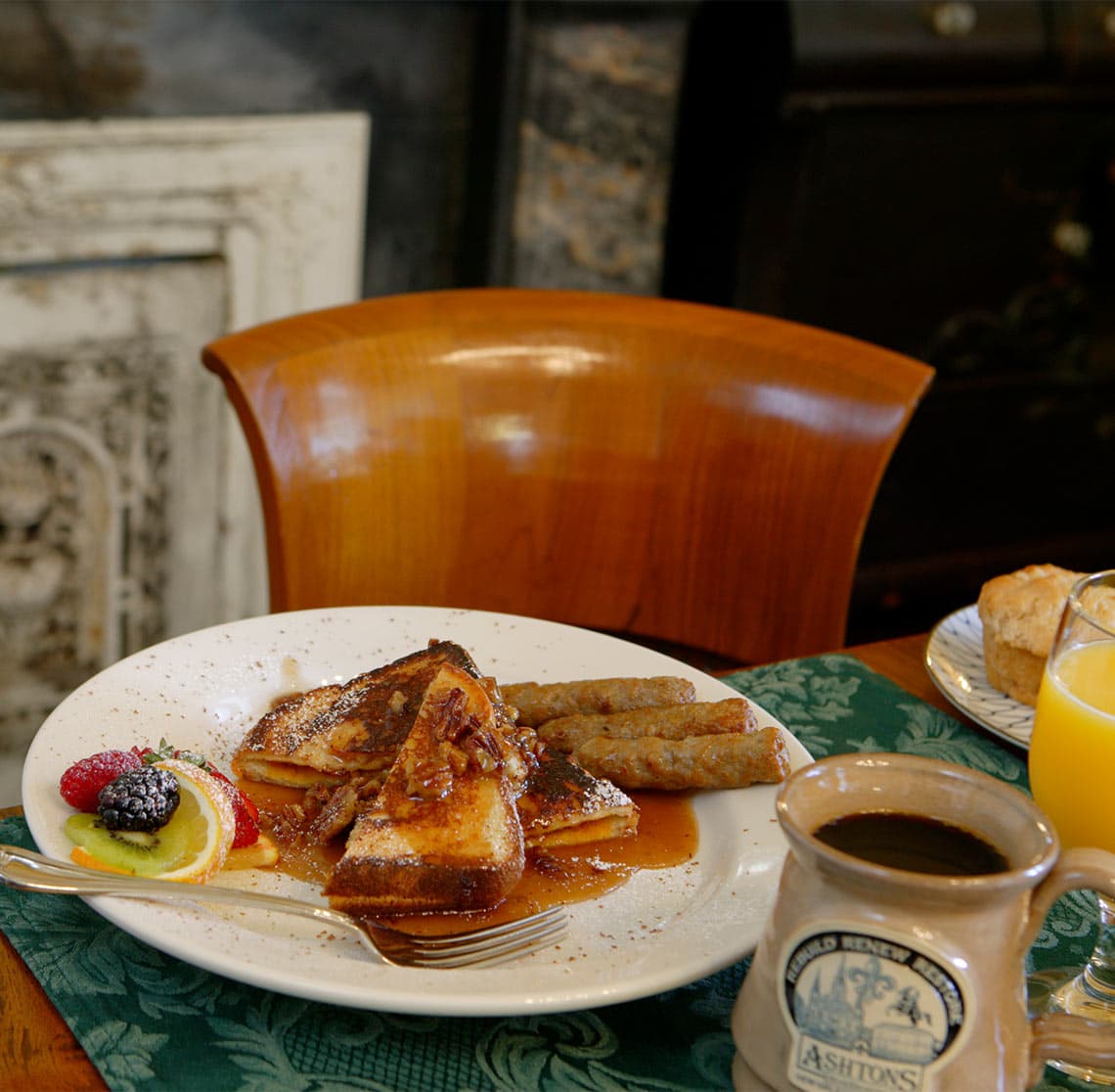 A plate of French toast with syrup, sausage, and fruit, accompanied by coffee and orange juice.